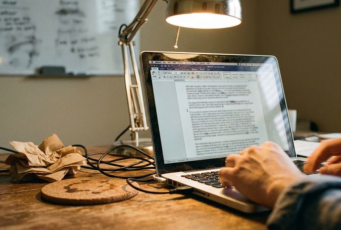 Home office writing setup with laptop displaying a text-heavy draft about NYC cooking habits